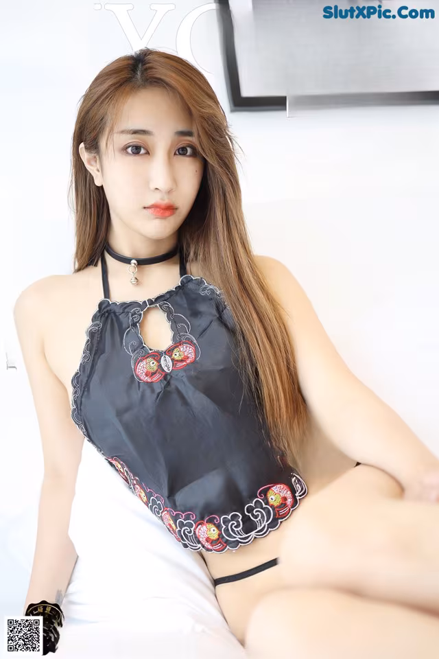 A woman in a black lingerie sitting on a bed.