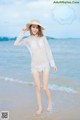 A woman in a white dress and hat standing on a beach.