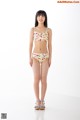A woman in a bikini standing in front of a white wall.