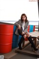 A woman sitting on top of a wooden bench next to a red barrel.