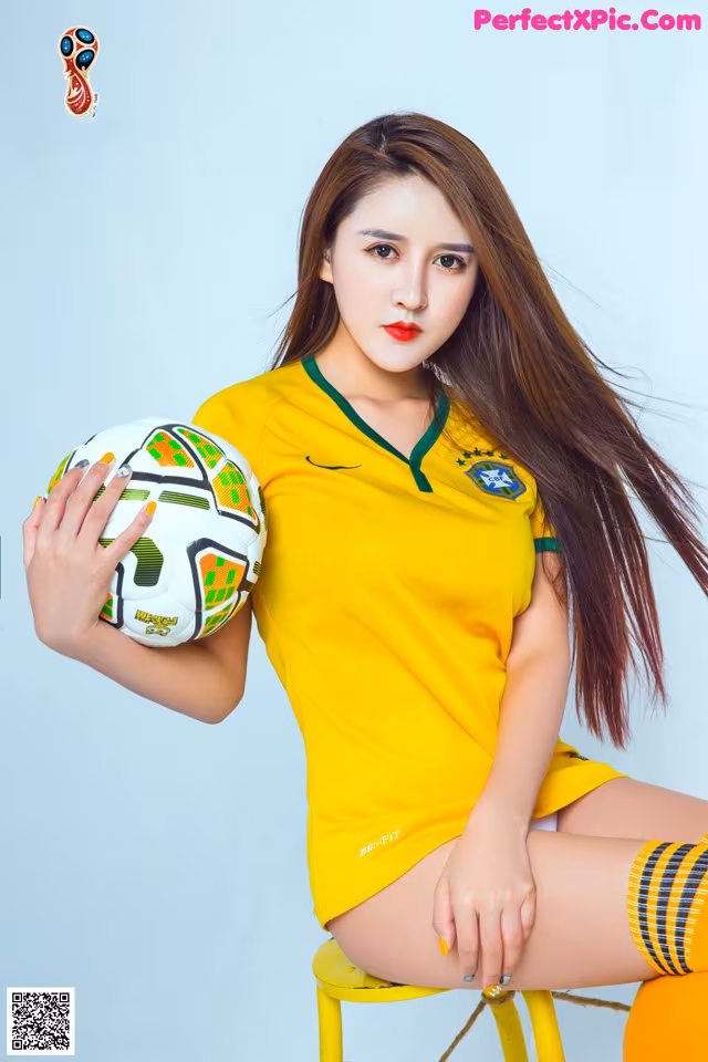 A woman in a yellow shirt holding a soccer ball.