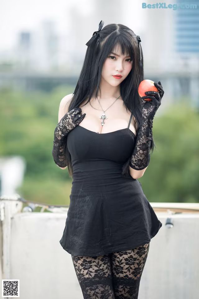 A woman in a black dress holding an apple.