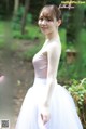 A woman in a white dress standing in the woods.