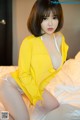 A woman in a yellow shirt is sitting on a bed.