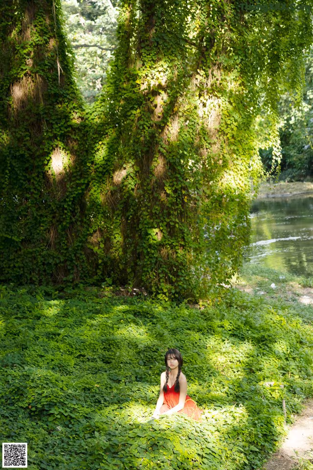 A woman in a red dress sitting under a tree.
