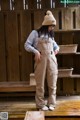 A woman standing on a wooden deck wearing overalls and a hat.