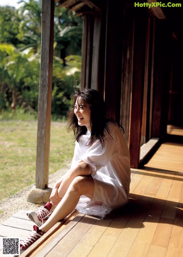 A woman sitting on a wooden porch with her legs crossed.