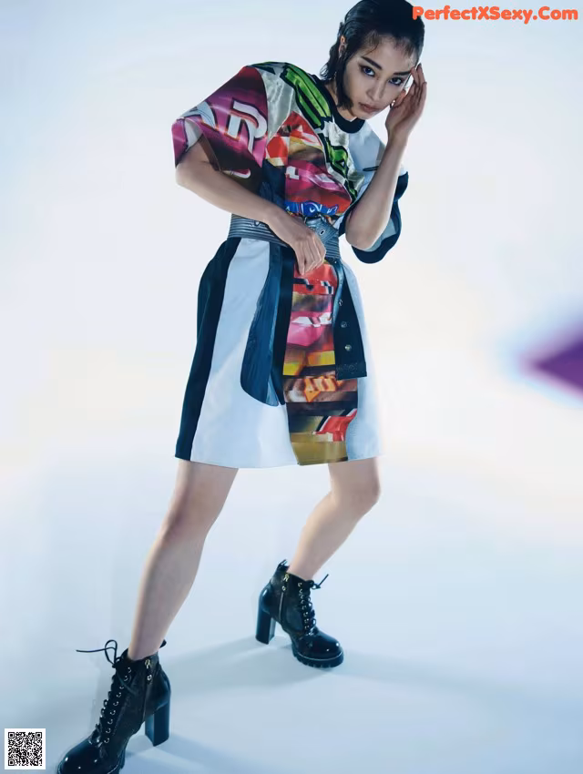 A woman in a colorful dress and black boots posing for a magazine.