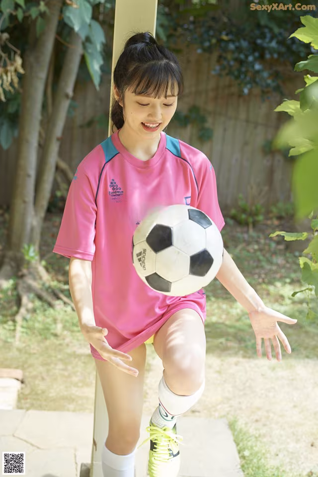 A young girl in a pink shirt kicking a soccer ball.