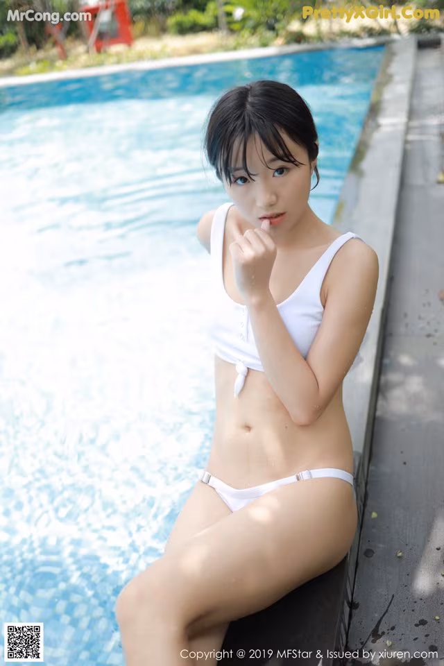 A woman in a white bikini sitting by a swimming pool.